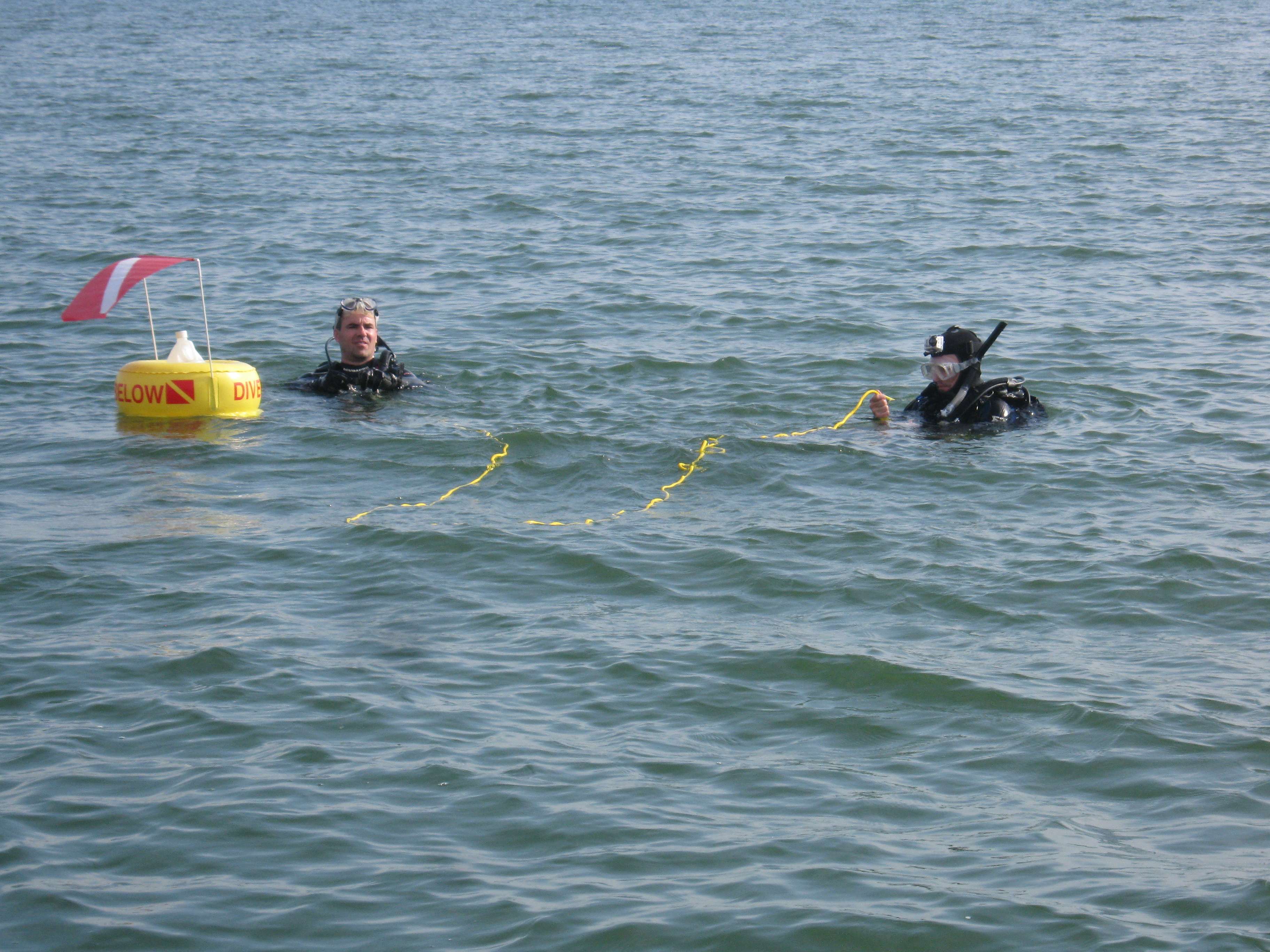 Two scuba divers mid-lake next to a caution buoy