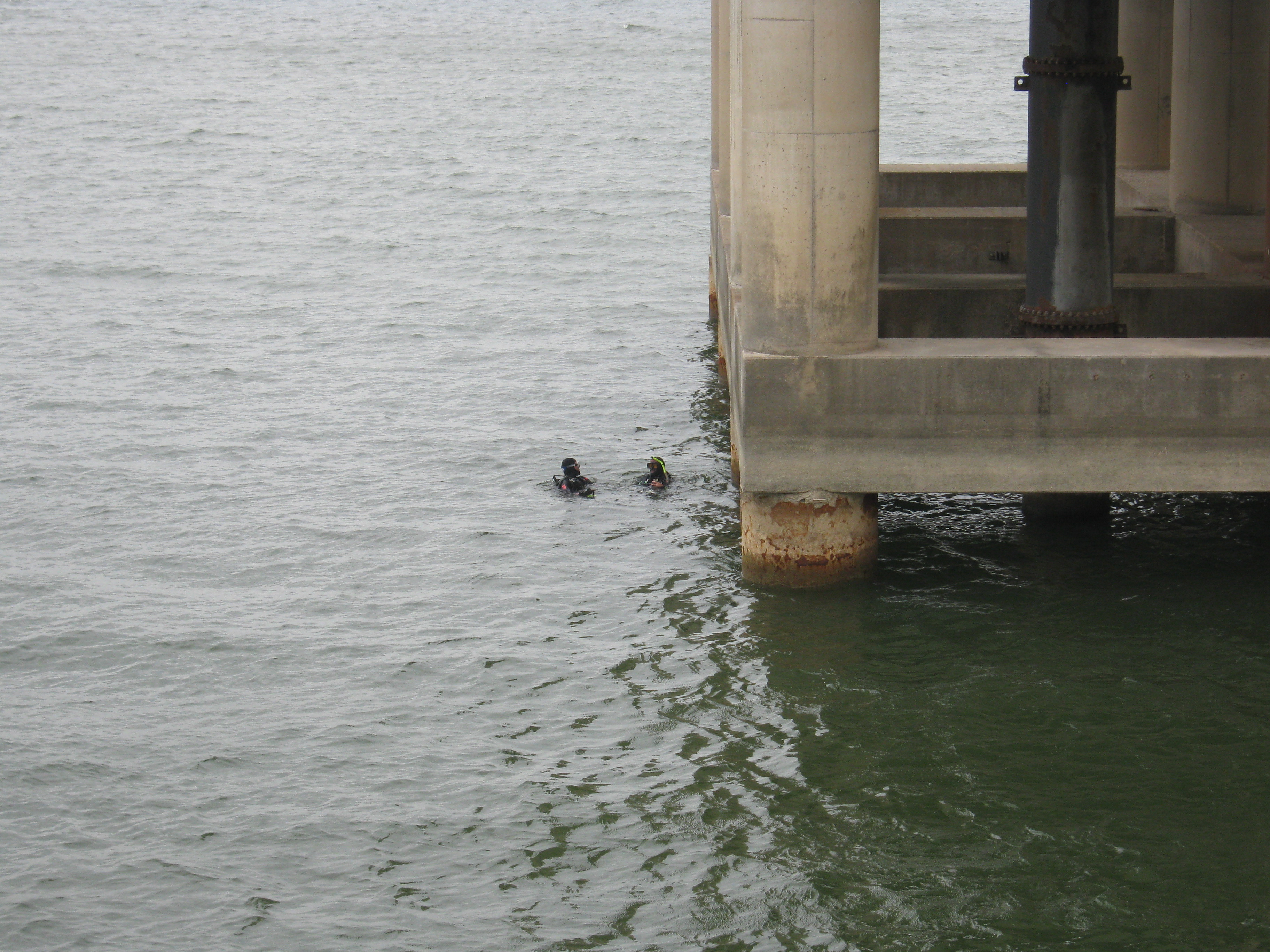 Two scuba divers, heads above water mid-photo, dwarfed by the concrete tower they will be inspecting