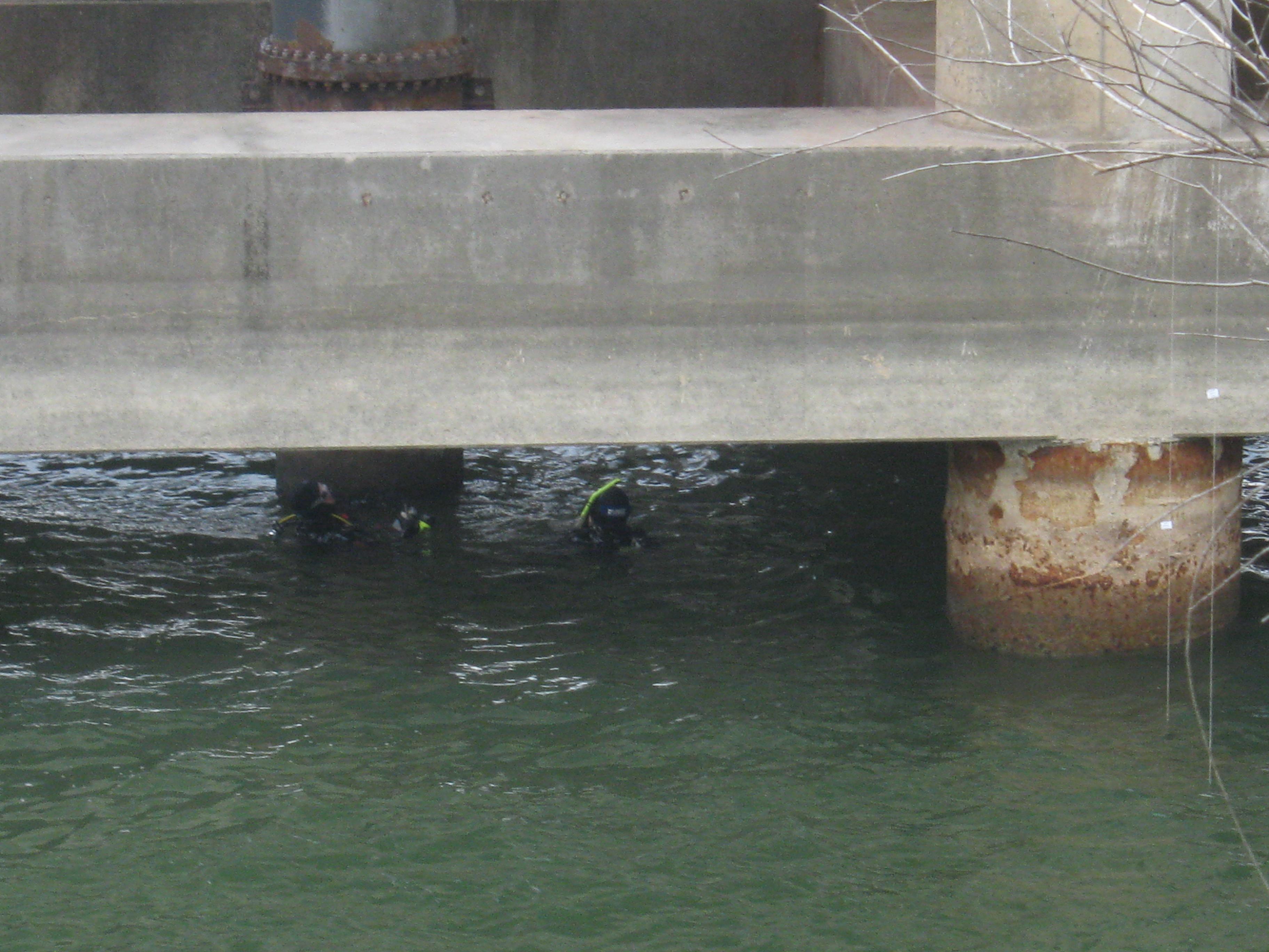 Scuba divers heads barely visible above the lake surface, under a large concrete structure