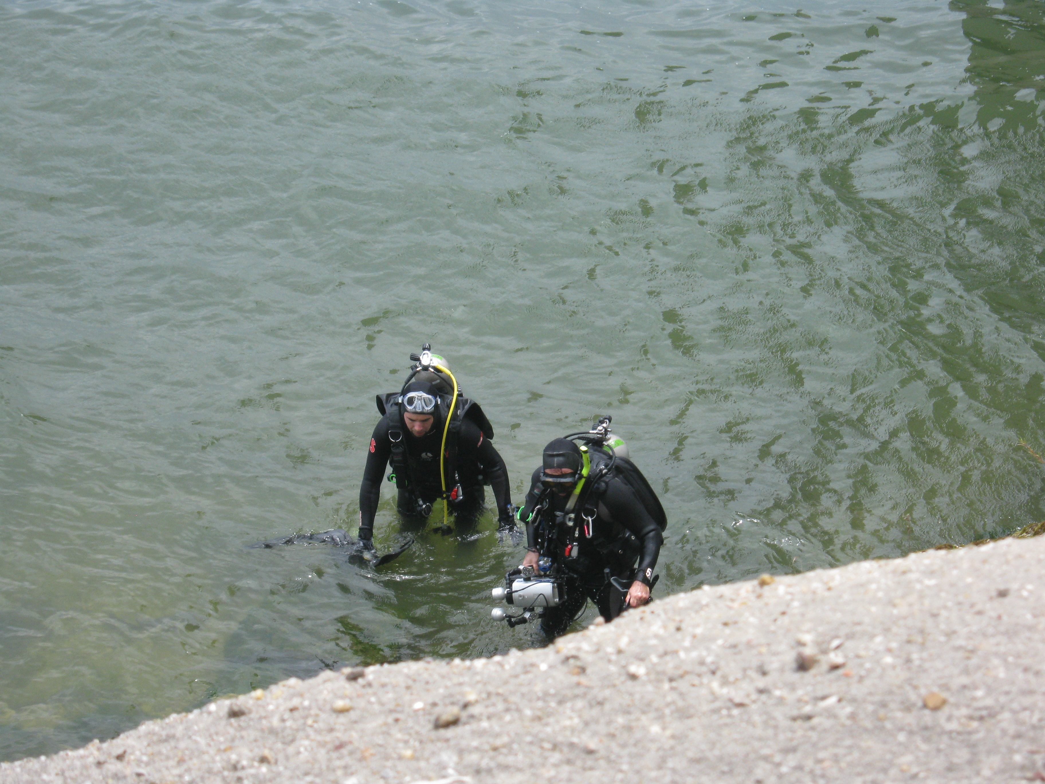 Two scuba divers stepping out of the water onto a rocky lake shore